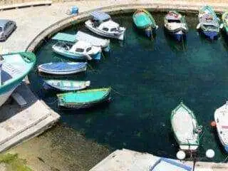 A high-angle view of small, colorful traditional fishing boats moored in the curved harbor area of Marsalforn.
