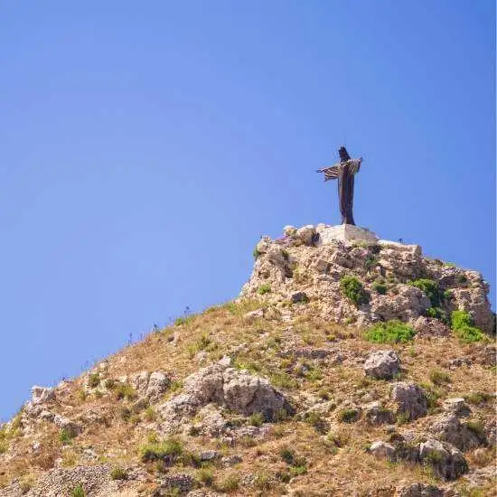 The iconic Tas-Salvatur statue (Risen Christ) standing atop the hill overlooking the Marsalforn valley against a clear blue sky.