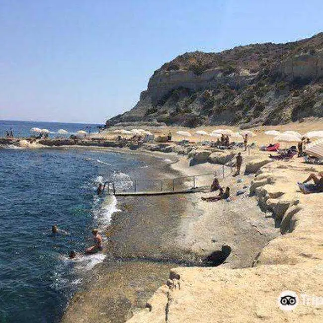 People sunbathing under white umbrellas and swimming at the rocky inlet of Għar Qawqla, a popular swimming spot with clay slopes near Marsalforn.