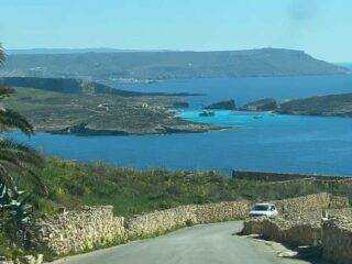 A scenic drive down the winding road towards Hondoq ir-Rummien Bay in Qala, offering panoramic views of the turquoise Blue Lagoon and Comino.