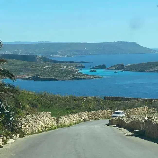 A scenic drive down the winding road towards Hondoq ir-Rummien Bay in Qala, offering panoramic views of the turquoise Blue Lagoon and Comino.