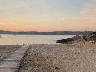 A wooden boardwalk leading down to the pebbly beach in Marsalforn Bay during a peaceful sunset, with calm waters in the background.