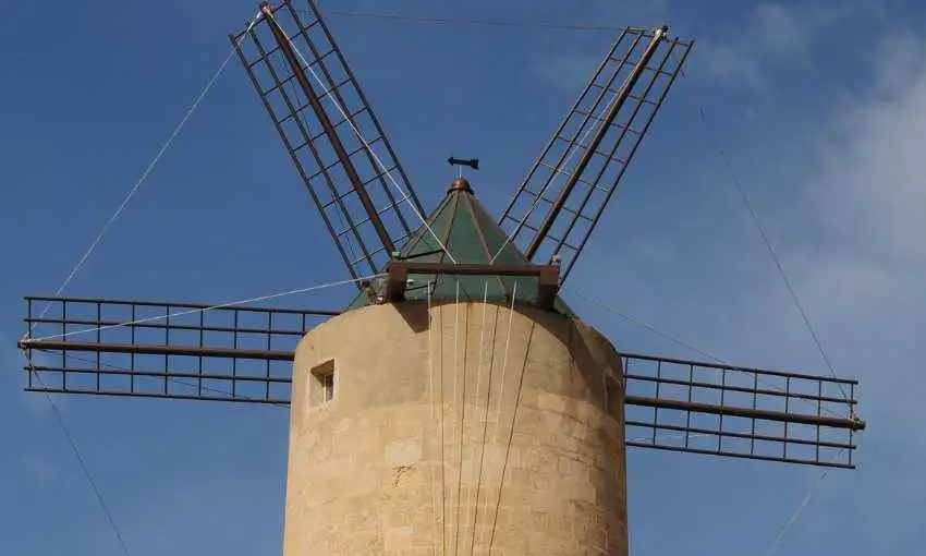 A close-up view of the historic Ta' Kola Windmill in Xaghra, featuring its traditional stone tower and wooden sails against a blue sky.