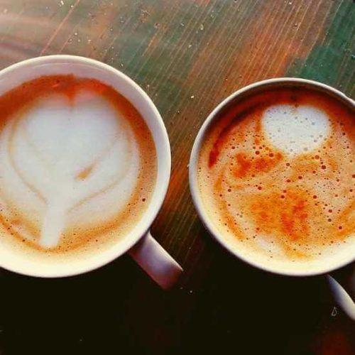 Two cups of coffee with latte art on a wooden table, capturing the relaxed café culture in Marsalforn.