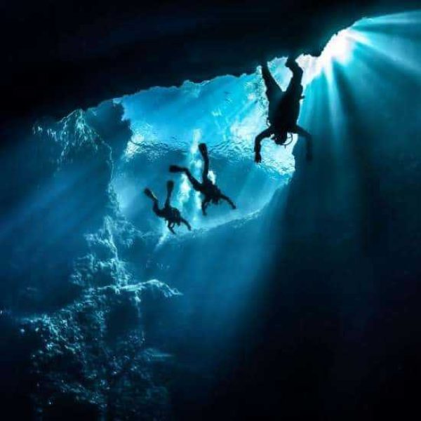 Three scuba divers silhouetted against the sunlight streaming into an underwater cave in Gozo.