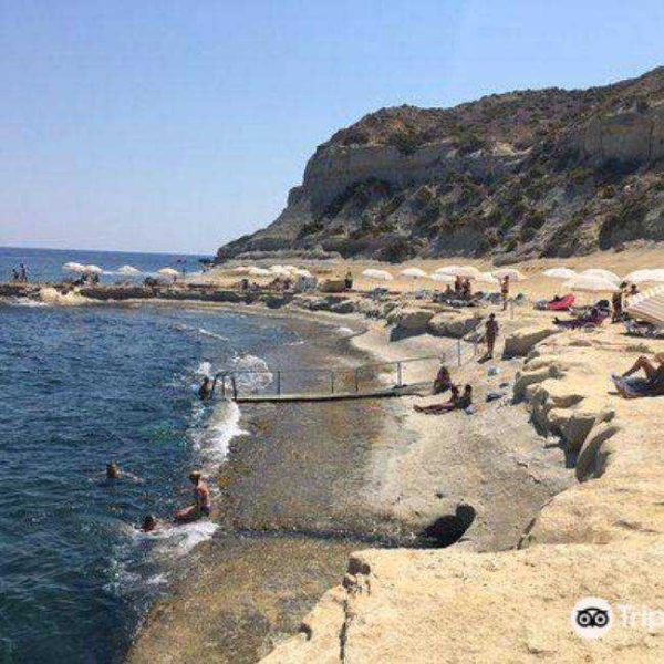 People sunbathing under white umbrellas and swimming at the rocky inlet of Għar Qawqla, a popular swimming spot with clay slopes near Marsalforn.