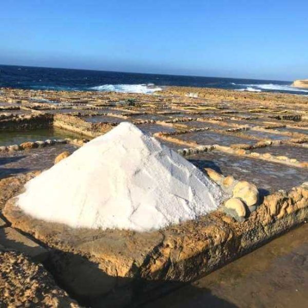A large pile of freshly harvested white sea salt sitting on the geometric, rock-cut Xwejni Salt Pans near Marsalforn.