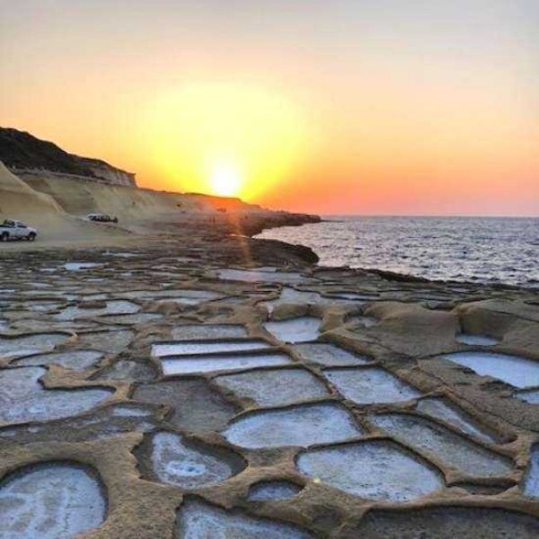 A breathtaking sunset casting a golden glow over the geometric rock-cut salt pans along the coast of Gozo near Marsalforn.